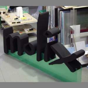 Lettere polistirolo verniciate Molix da 40 cm, dipinte di nero. Supporto a rampa in plexiglass trasparente dove sono fissate le lettere.